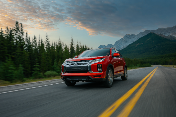 A red RVR driving on a country road with a mountain in the background