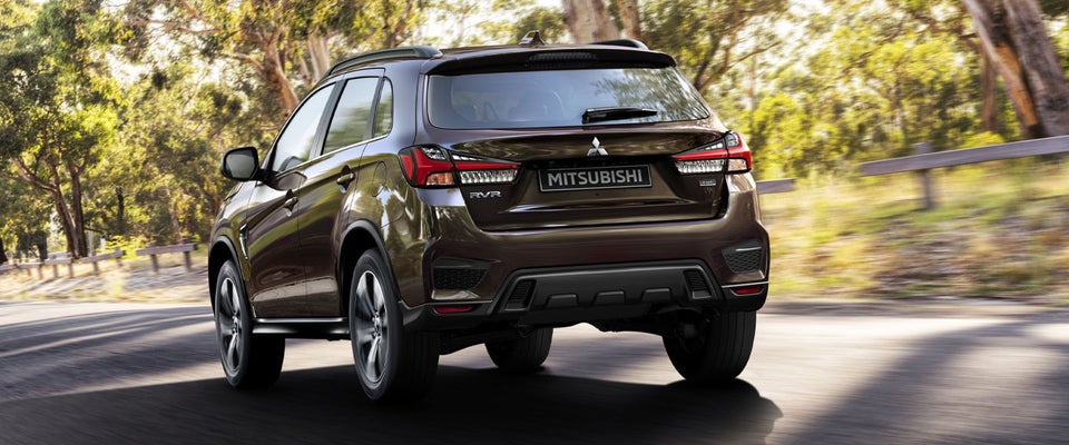 Rear and side view of a 2024 Mitsubishi RVR driving fast on a mountainous road.